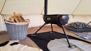 A tent with a portable stove, a basket of firewood, and a patterned rug.