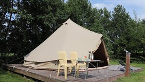 A tent with a table and chairs set up on a wooden platform in a grassy area with trees in the background.