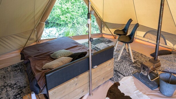 A tent with a bed, a chair, a heater, and a bucket.