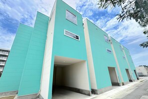 Un edificio moderno con fachada verde azulado, múltiples ventanas y una entrada central.