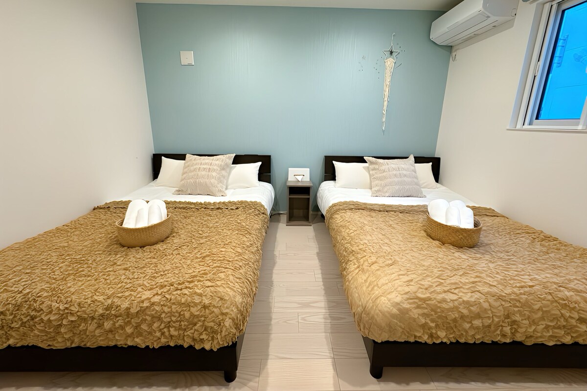 A twin bedroom with two beds, each with a textured beige bedspread and a woven basket on the footboard.
