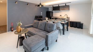 A modern living room with a grey sofa, a dining table set for two, and a kitchen area with a black refrigerator and microwave. - Grandioso Okinawa Pool Villa Kin 2 (Kin)
