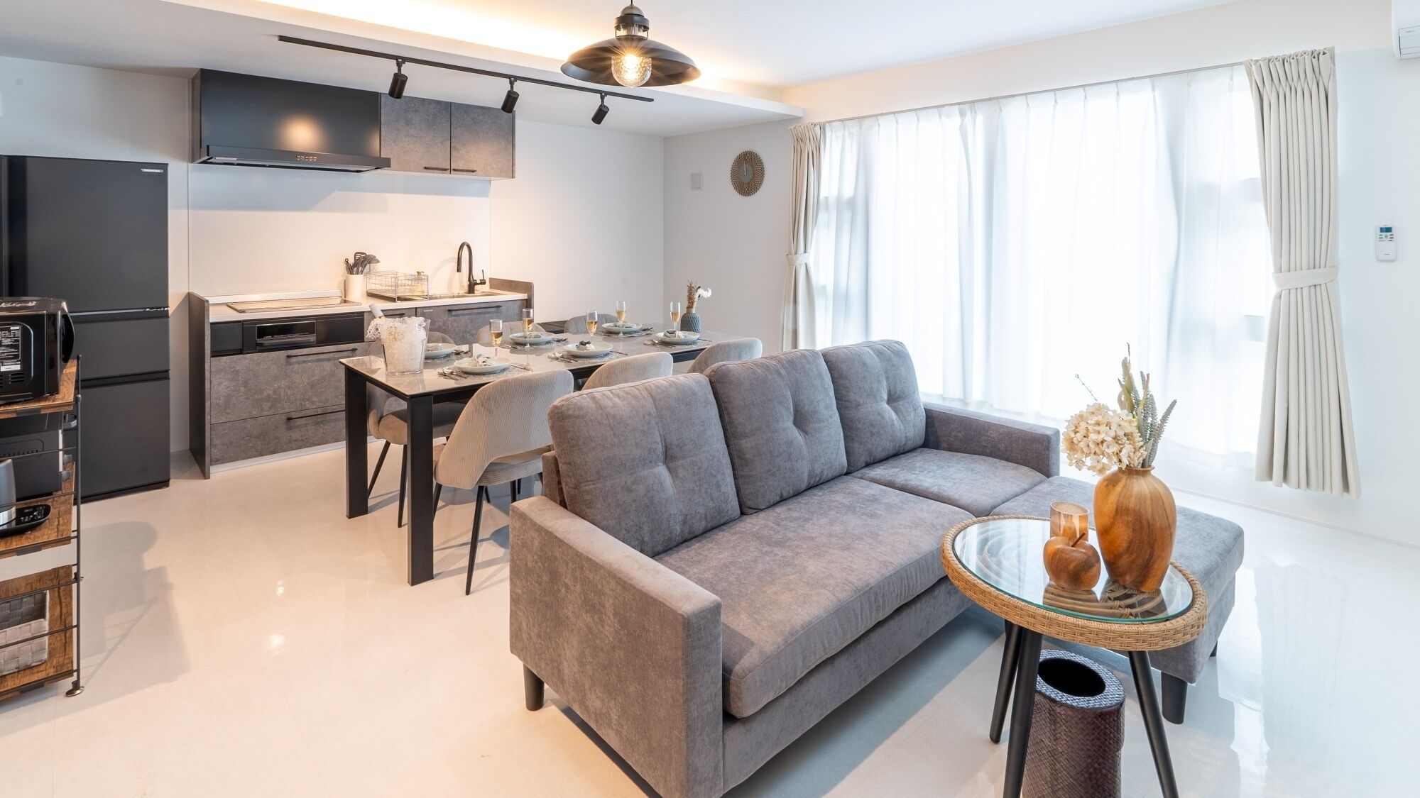 Ein modernes Wohnzimmer mit einem grauen Sofa, einem Esstisch für zwei Personen und einer Küche im Hintergrund.