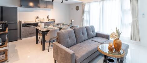 Una sala de estar moderna con un sofá gris, una mesa de comedor para dos personas y una cocina al fondo.