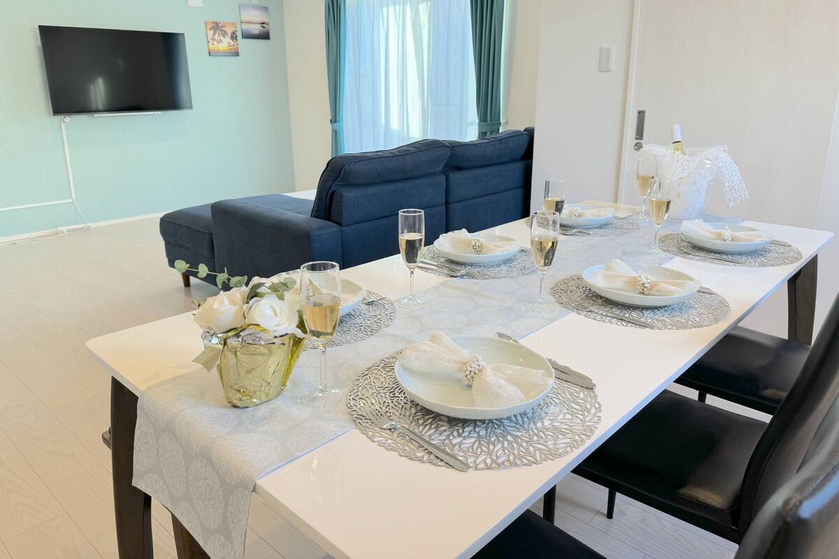 A dining area with a table set for four, a sofa, and a flat-screen TV mounted on the wall.