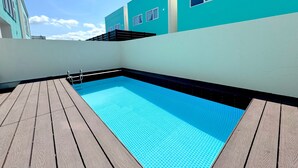 A rooftop swimming pool with a wooden deck, surrounded by turquoise buildings. - Grandioso Okinawa Pool Villa Kin 2 (Kin)