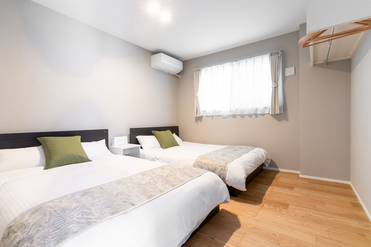 A hotel room with two beds, a window with curtains, an air conditioning unit, and a wooden floor.