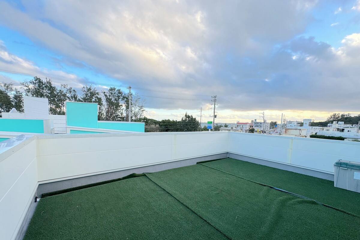 A rooftop terrace with artificial grass, white walls, and a view of the cityscape.