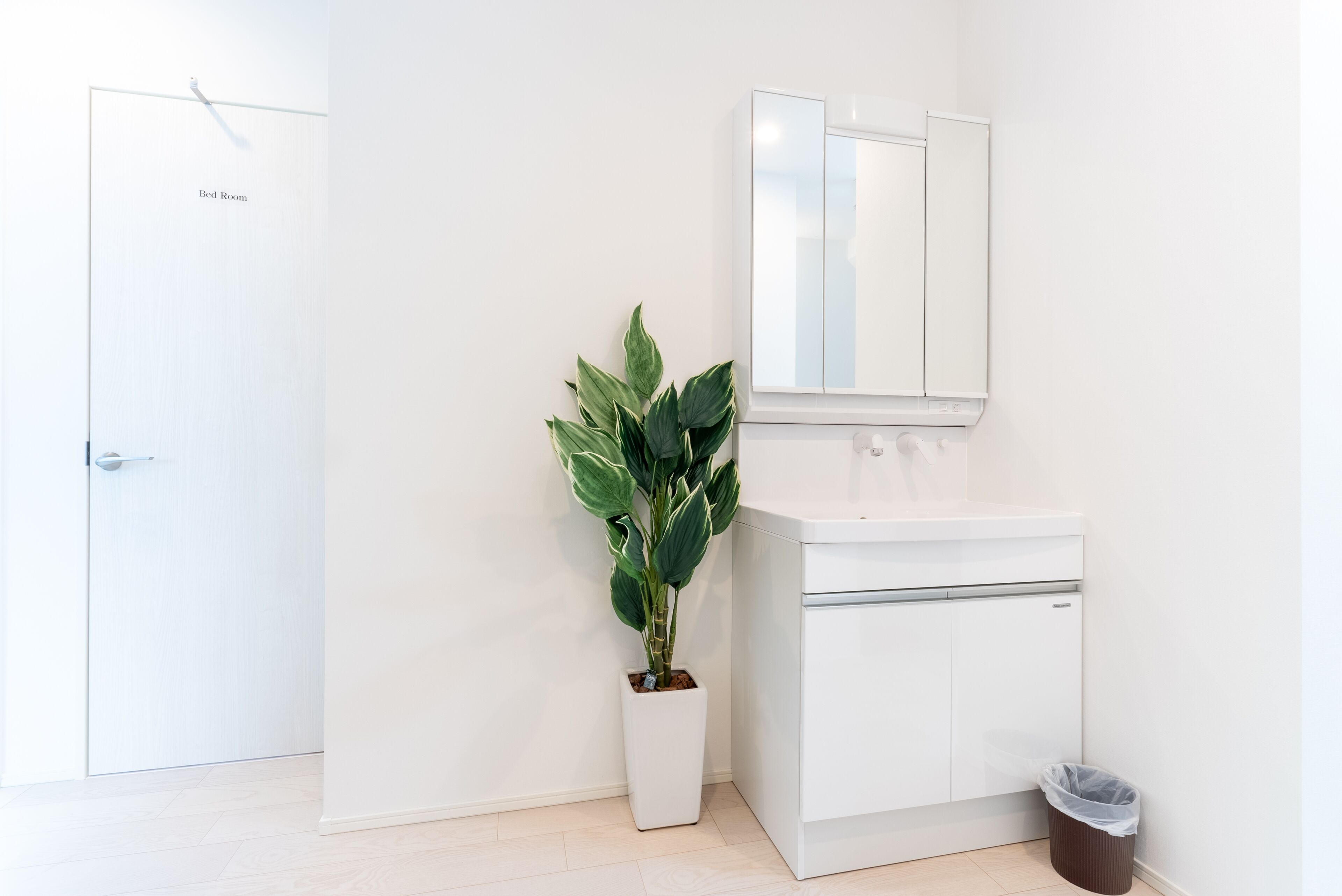 A clean, white bathroom with a large mirror, a white sink, and a potted plant.