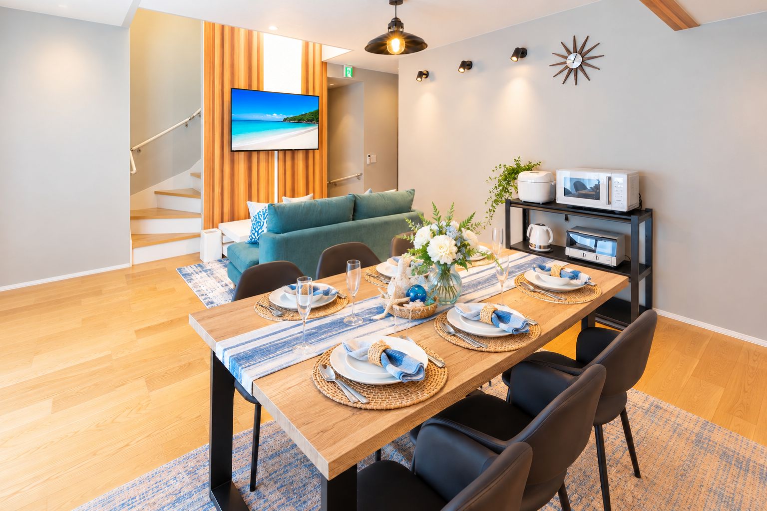 Un comedor con una mesa de madera preparada para cuatro, un sofá y un televisor al fondo.