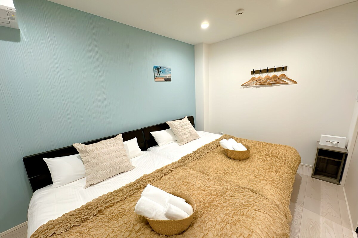A neatly made bed with a textured blanket and pillows, a small wall-mounted shelf with hangers, and a framed picture on the wall.