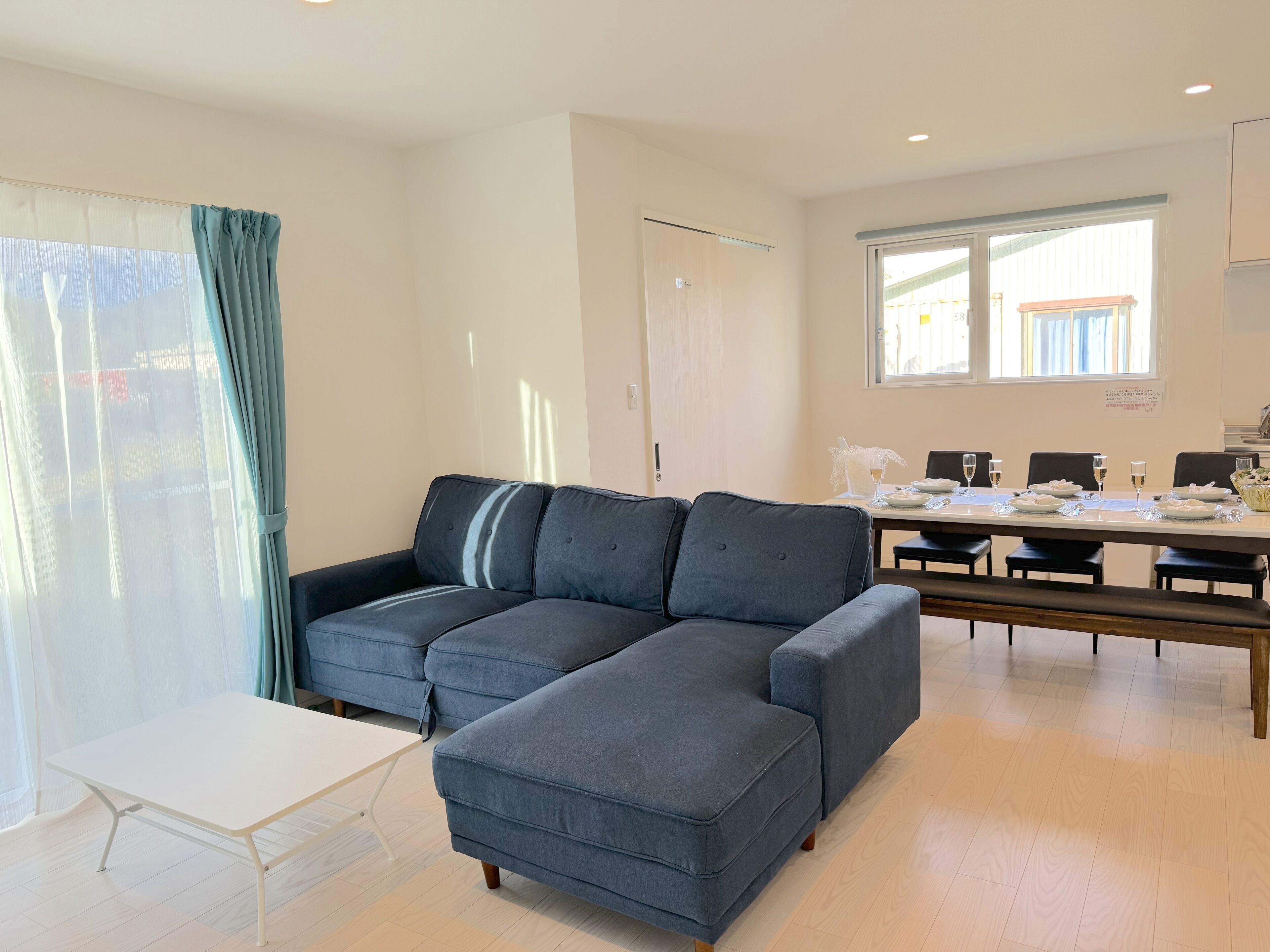 A modern living room with a grey sectional sofa, a white coffee table, and a dining area with a table set for four.