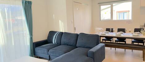 A modern living room with a grey sectional sofa, a white coffee table, and a dining area with a table set for four.