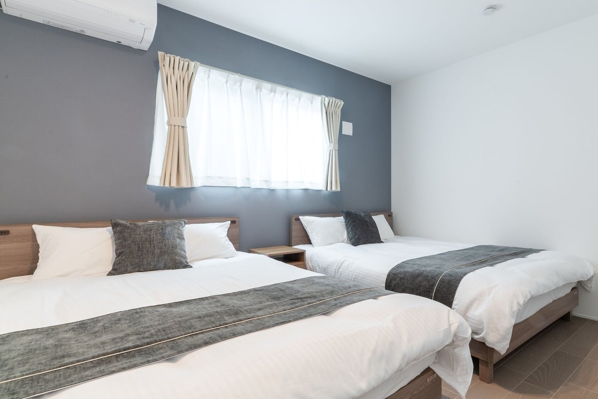 A hotel room with two beds, a window with curtains, a wall-mounted air conditioner, and a tiled floor.