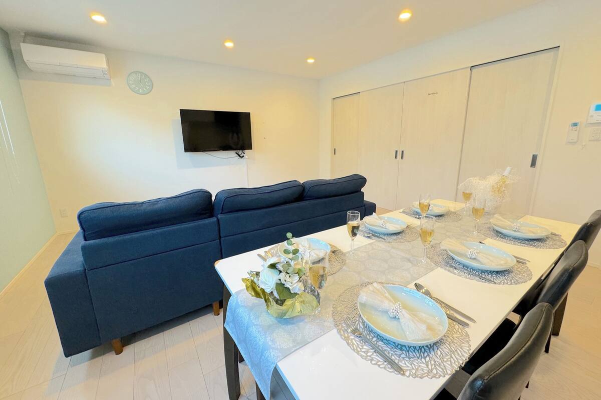 A dining area with a table set for four, a blue sofa, a flat-screen TV on the wall, and a wardrobe.