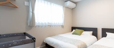 Habitación de hotel con dos camas, una mesita pequeña, un perchero de madera y una ventana con cortinas.