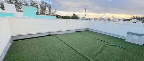 Une terrasse avec un revêtement de gazon synthétique, des murs blancs et une vue sur les bâtiments au loin.