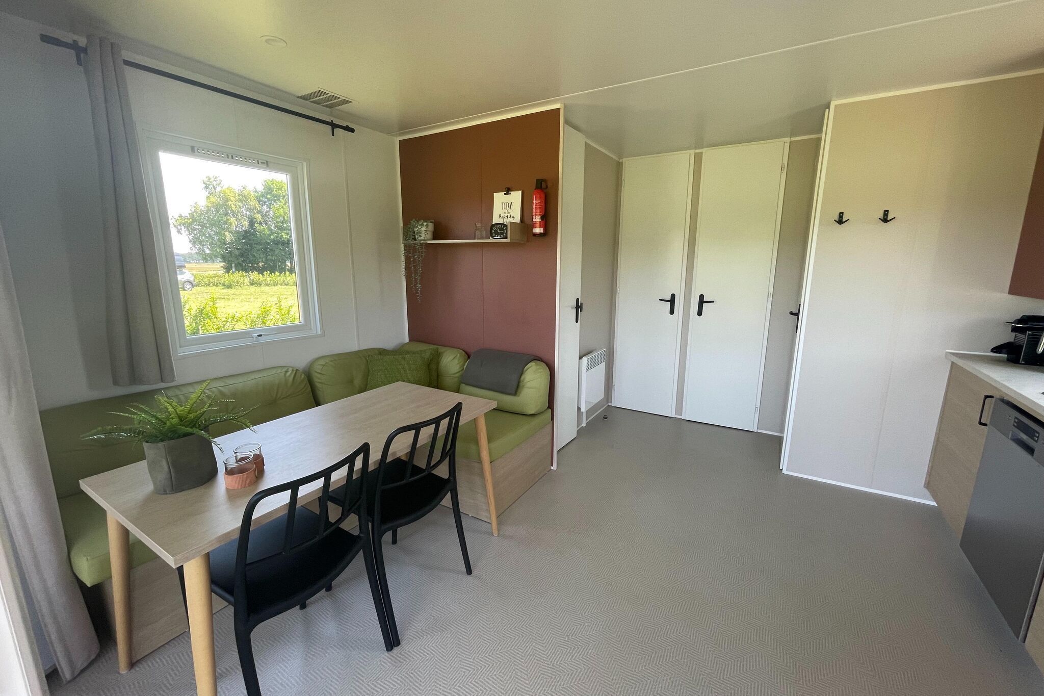 A compact kitchen with a dining area, a green sofa, and a window with a view of greenery.