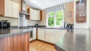 A kitchen with a central island, a stove, a microwave, and a window with a view of greenery. - Stylish luxury lodge with meadow view. (Wattleborough, Nr Shrewsbury)