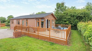 A wooden cabin with a deck, a small pool, and a garden area. - Stylish luxury lodge with meadow view. (Wattleborough, Nr Shrewsbury)