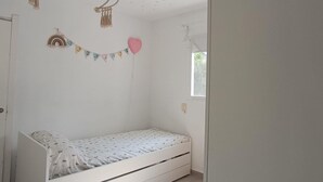 Quarto pequeno com uma cama de solteiro, roupa de cama branca, uma decoração em formato de coração, uma guirlanda de bandeirinhas coloridas e um teto com desenhos de estrelas.