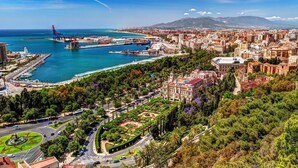 Paisagem costeira com um porto de iates, edifícios históricos e um parque com uma fonte em forma de estrela.