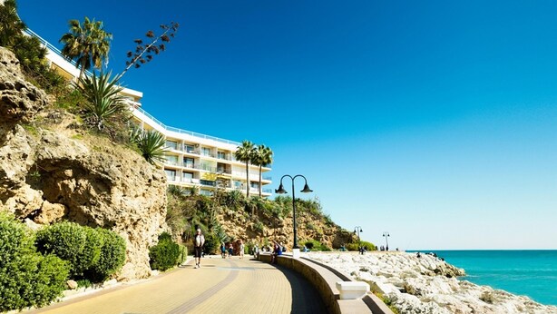 Hotel à beira-mar com um caminho sinuoso que leva à praia, rodeado por terreno rochoso e palmeiras.