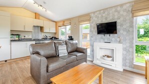 A modern living room with a sofa, a wooden coffee table, a fireplace, and a kitchen area with cabinets and appliances.