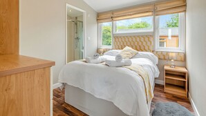 A bedroom with a bed, bedside tables, a wooden bench, a window with curtains, and a shower area.