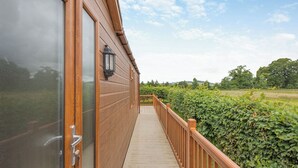 A wooden deck with a railing, a glass door, and a view of a green hedge and sky.