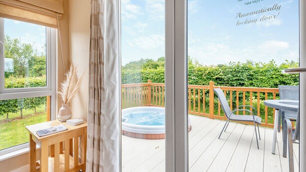 A balcony with a hot tub, wooden deck, and a view of greenery.