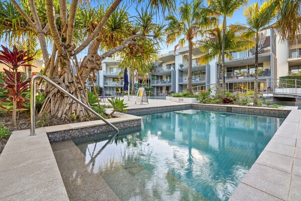 Relax by the serene pool surrounded by lush tropical vegetation and palm trees.