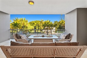 Relax on the balcony with a view of the lush garden, featuring a table and wicker furniture.