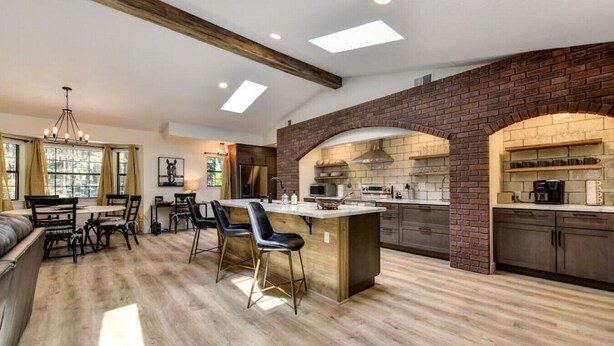 A spacious kitchen with a central island, exposed brick walls, and a dining area with a wooden bench and chairs. - Harmony Ridge Ranch Nevada City (Nevada City)