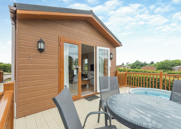 Um deck de madeira com porta de vidro que dá para uma cozinha, piscina e móveis de exterior.