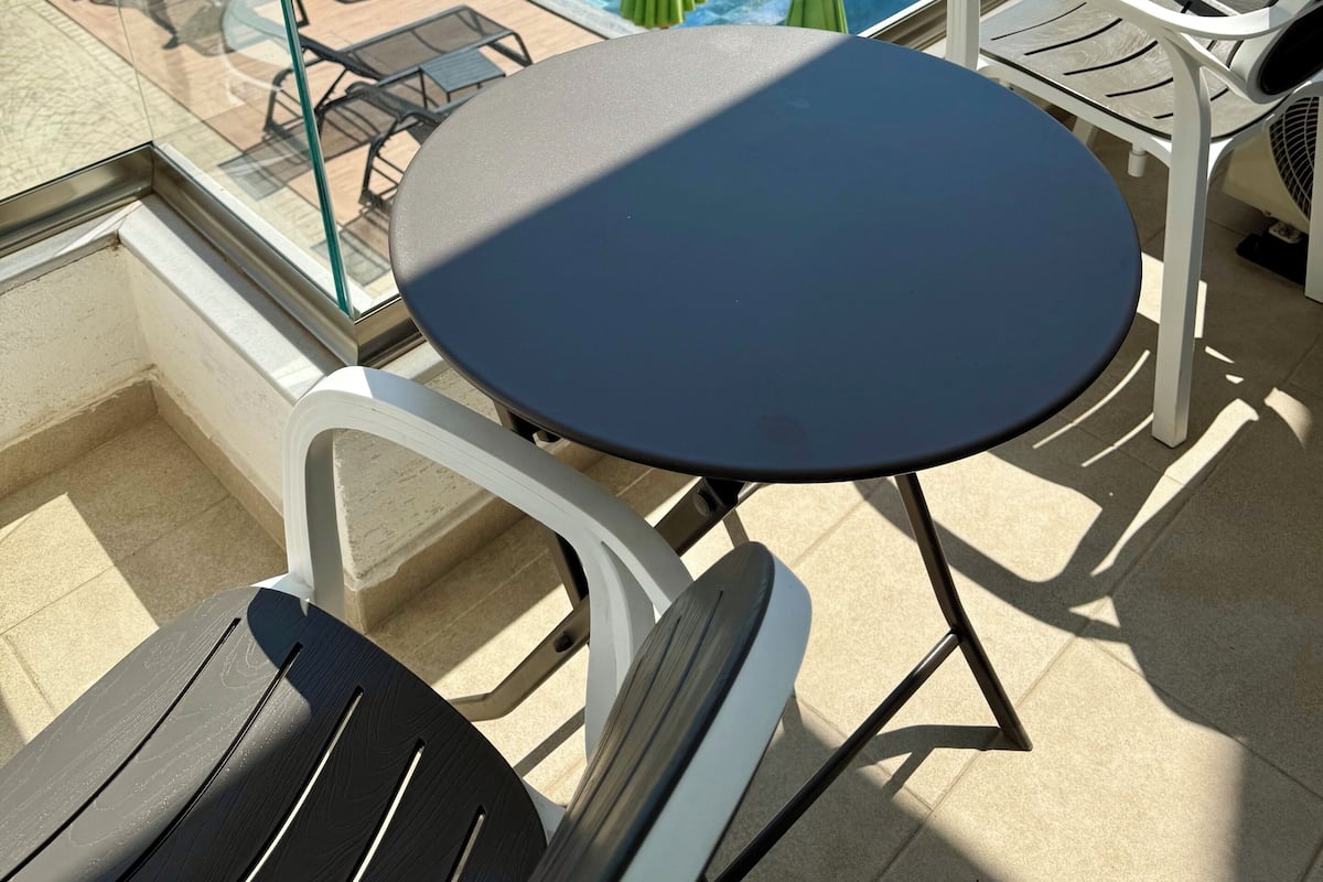 Área da piscina com espreguiçadeiras, mesa e guarda-sóis, com vista para um lago e colinas.