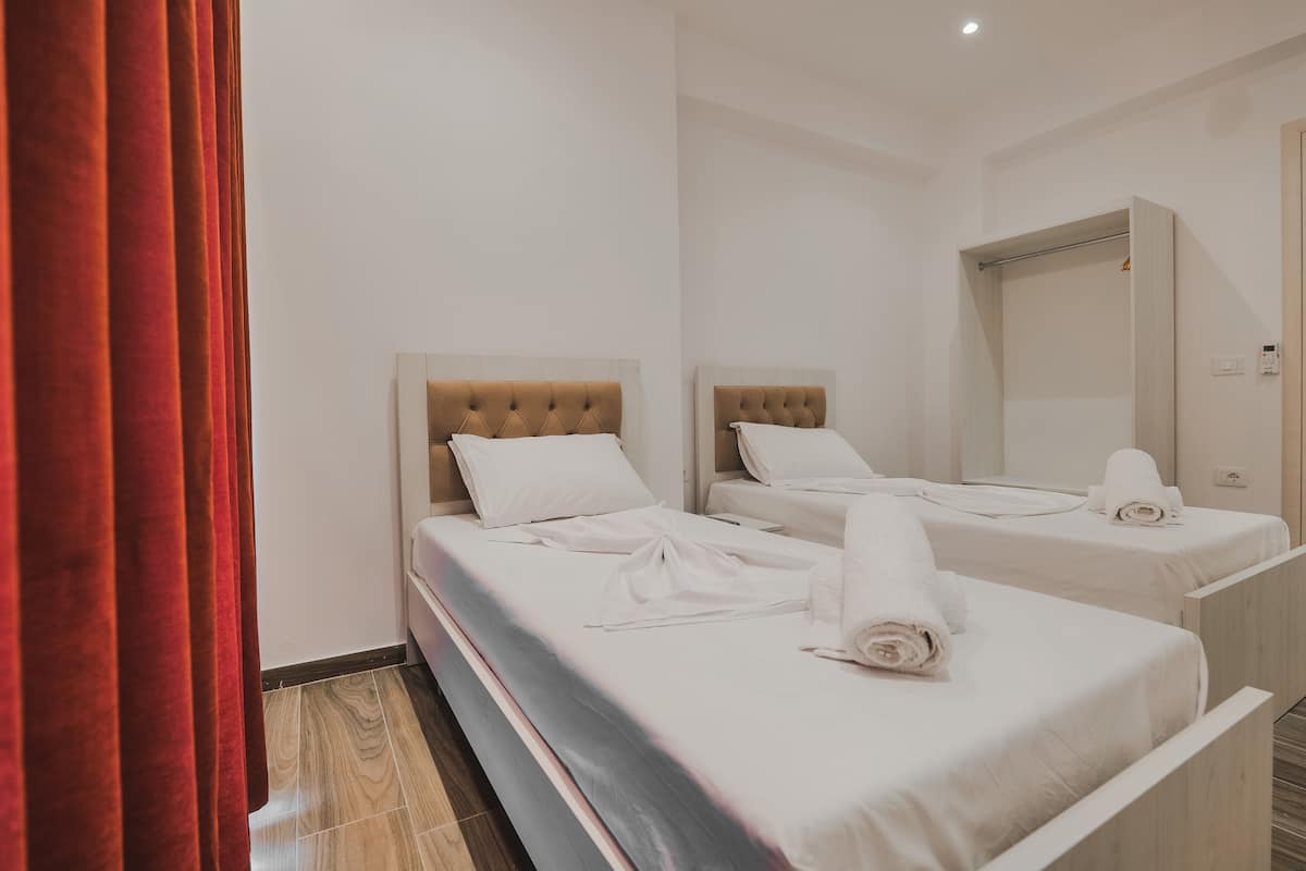 Quarto de hotel com duas camas, cada uma com cabeceira e roupa de cama branca.