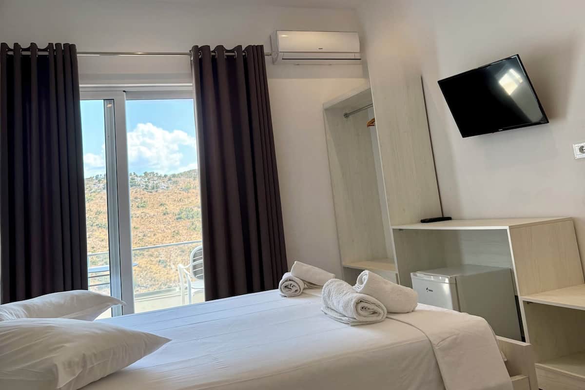 Quarto de hotel com cama, televisão, aparelho de ar condicionado e vista para o exterior.