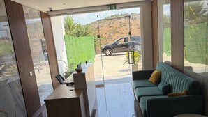 Un interior moderno con un mostrador de recepción, un sofá y vistas a un coche y zonas verdes al exterior.