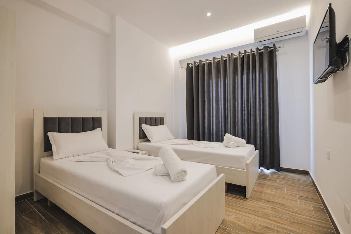 Quarto de hotel com duas camas, televisão de tela plana na parede e janela com cortinas escuras.