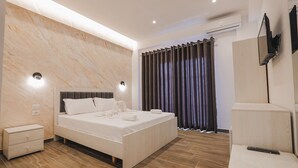 Un dormitorio moderno con una cama grande, mesitas de noche, televisor montado en la pared y una ventana con cortinas.