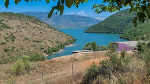 Un paisaje montañoso con un lago, un puente y un edificio pequeño con techo púrpura.