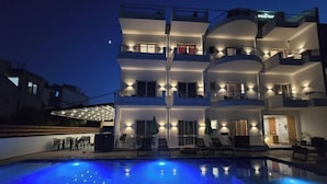 Un hotel de varios pisos con piscina, mobiliario exterior y fachada bien iluminada.