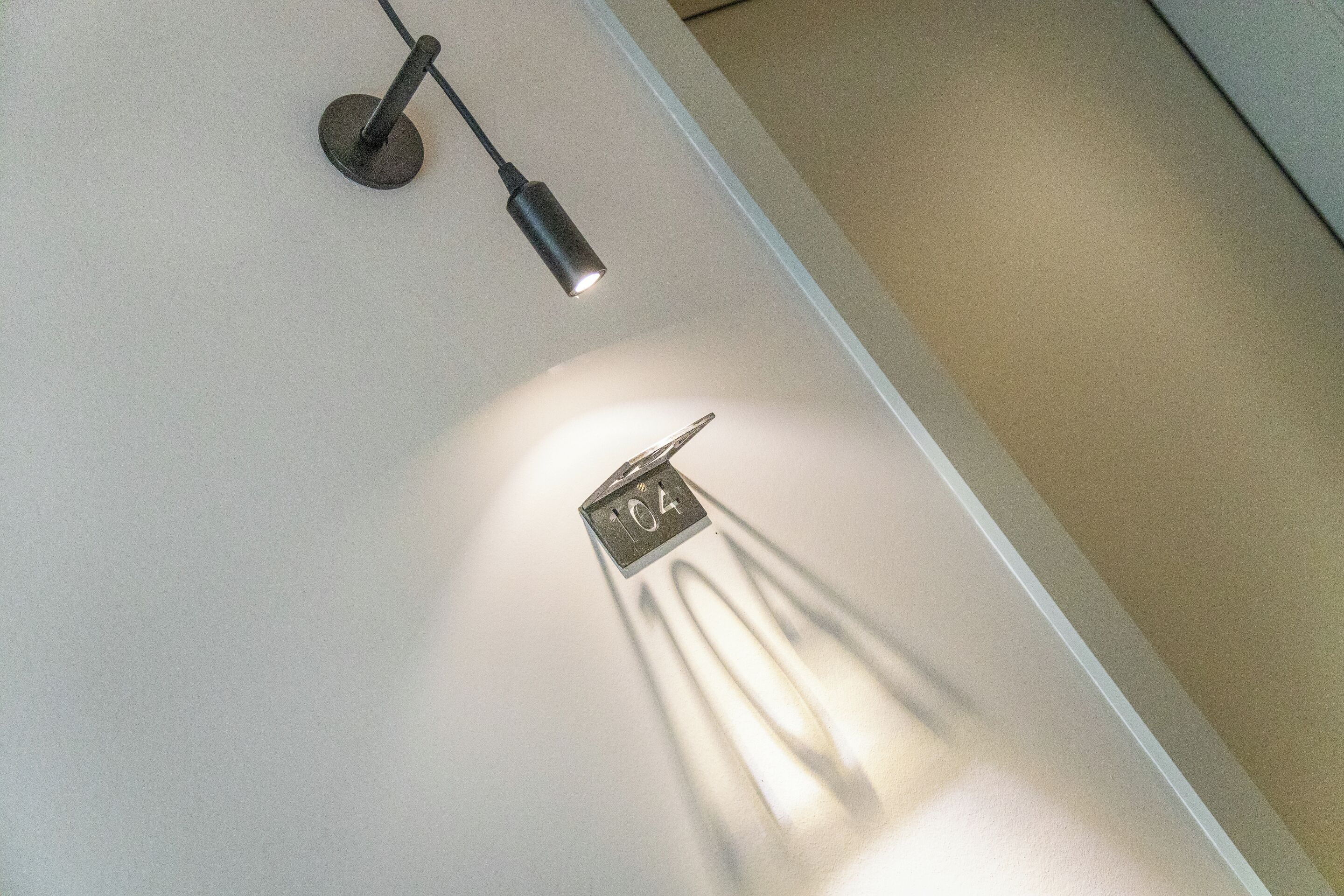 Una lámpara fijada al techo con el número '104' visible y una sombra proyectada en la pared.