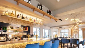 A bar area with wooden shelves, blue bar stools, and a variety of bottles and glasses.