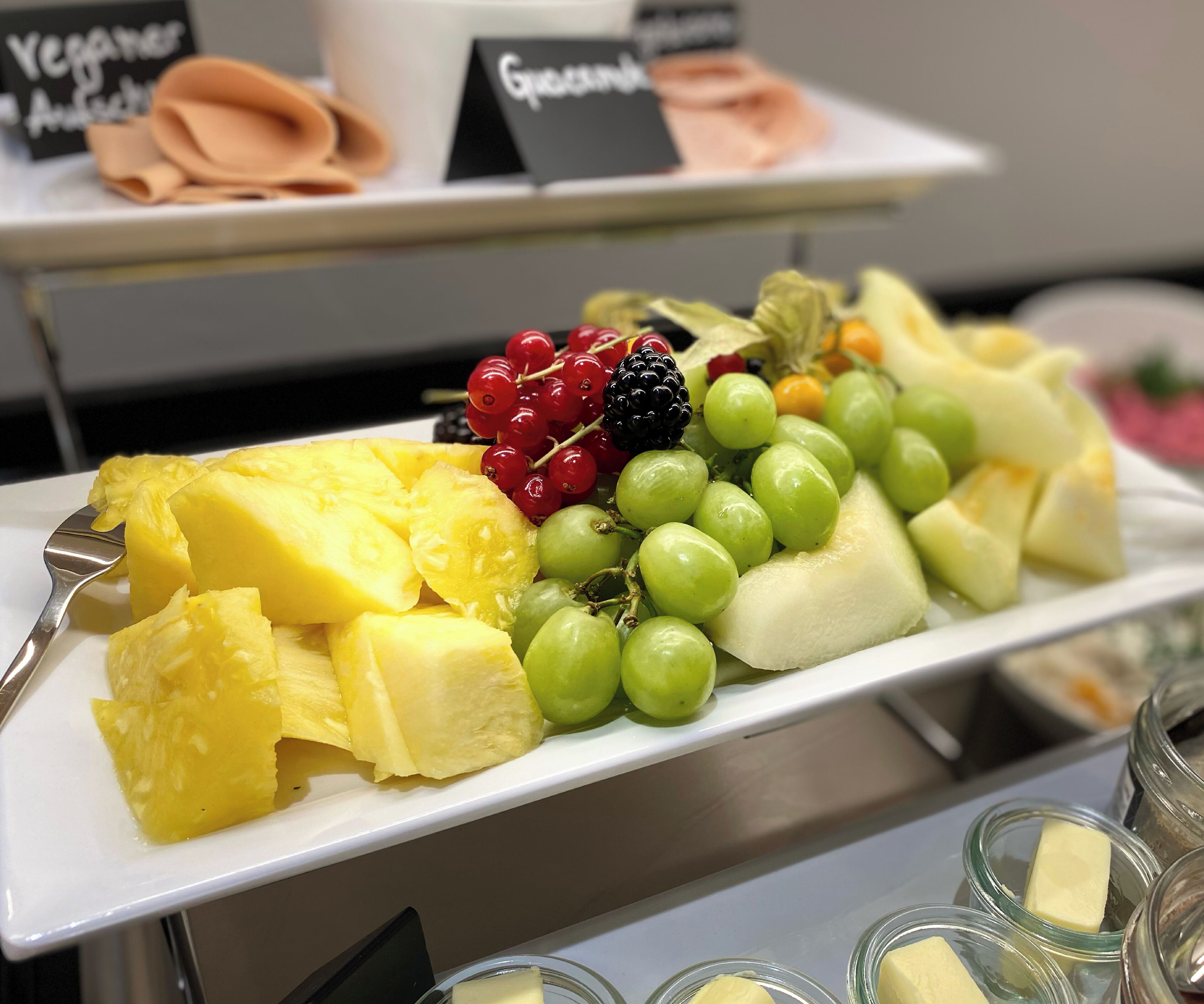 A fruit platter with pineapple, grapes, and berries on a white plate.