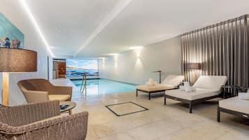 Un espace piscine intérieur moderne, doté de chaises longues, d’un grand tableau et offrant une vue sur la piscine.