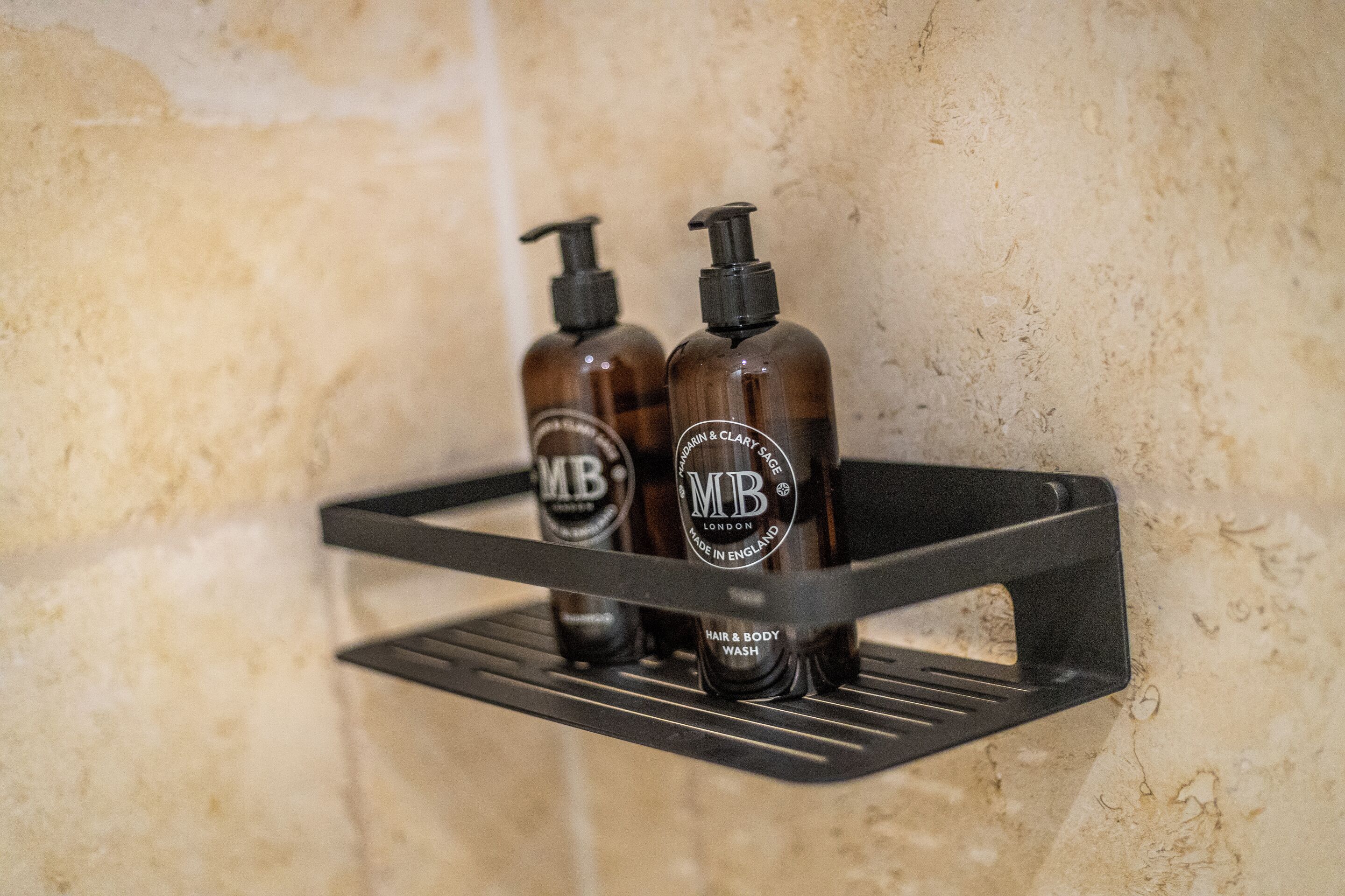 Two bottles of hair and body wash on a black metal shelf against a textured wall.