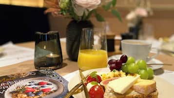 Une table dressée pour le petit-déjeuner, avec une assiette de toasts, des fruits, un verre de jus d’orange, une bougie et une tasse de café.