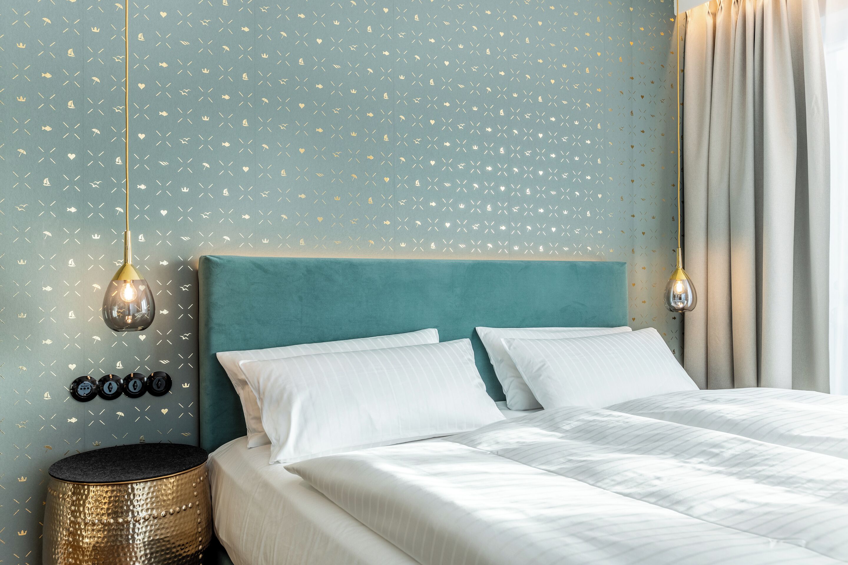 A neatly made bed with white linens, a teal headboard, and a round gold side table.